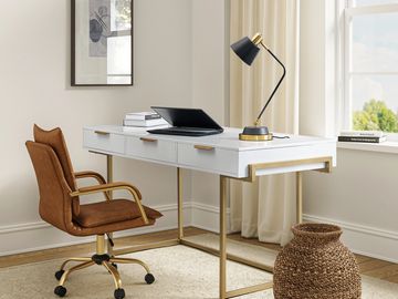 Elegant home office with a white desk, leather chair, and gold-accented lamp.