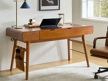A stylish wooden desk with modern lamp, laptop, and accessories in a bright office space.