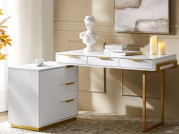 Elegant white and gold desk with drawers, decorated with books, candles, and a bust sculpture.