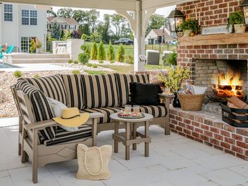 Cozy outdoor patio with striped cushioned seating and a lit brick fireplace.