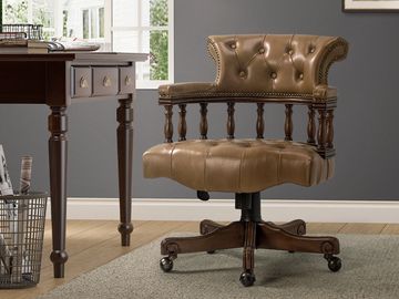 Classic brown leather office chair with wooden frame on a carpet near a desk.