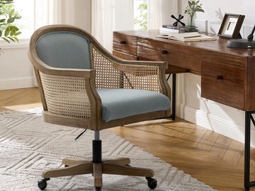 A wooden office chair with blue cushions on a textured rug beside a wooden desk.