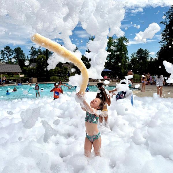 Child playing joyfully in a pool filled with foam bubbles.