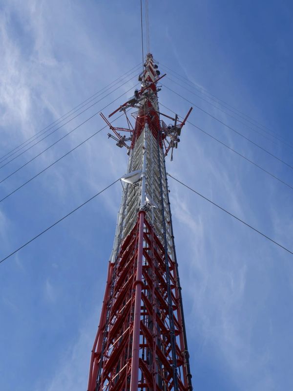 Tall red and white communication tower against a blue sky.