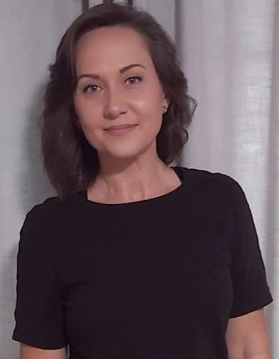 Smiling woman in black shirt stands in front of curtain.
