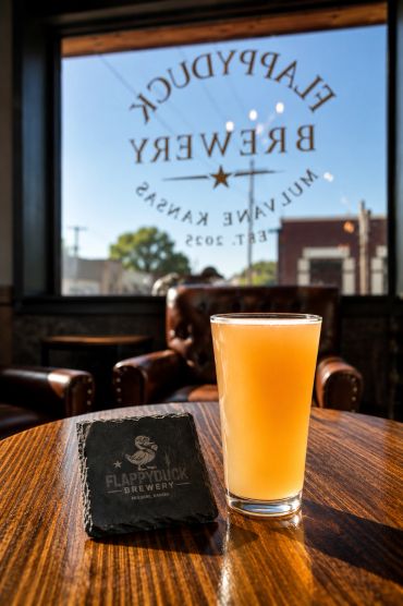 A glass of beer and a brewery coaster on a wooden table.