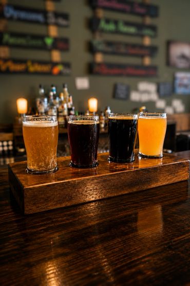 Four different beers on a wooden flight paddle at a bar.