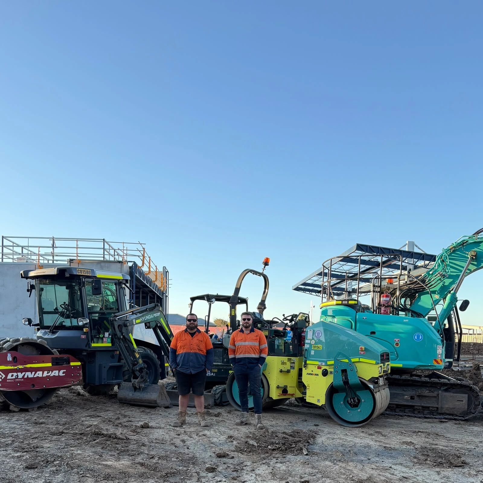 Two construction workers standing among heavy machinery at a construction site.