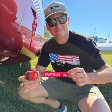 Man holding a 'REMOVE BEFORE FLIGHT' tag near a red helicopter.