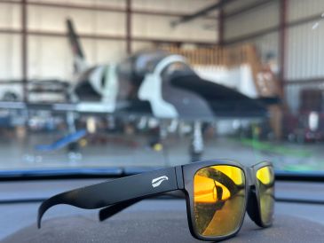 Yellow-lensed sunglasses on a dashboard with a blurred airplane in the background.