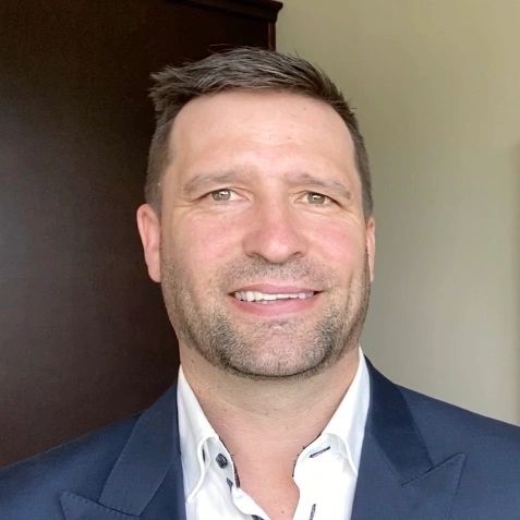 Smiling man in a navy blue suit and white shirt.