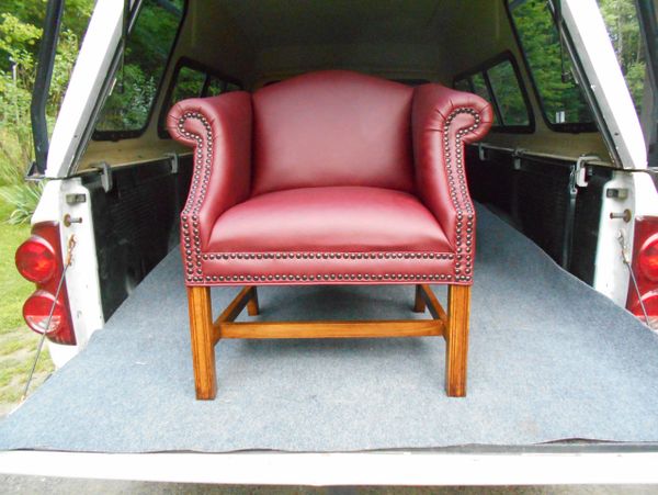 A red leather armchair with wooden legs in the back of a vehicle.
