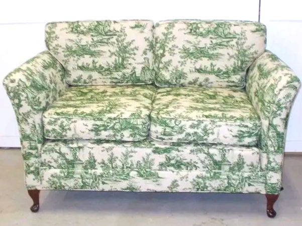 A vintage two-seater sofa with green and white pastoral print upholstery.