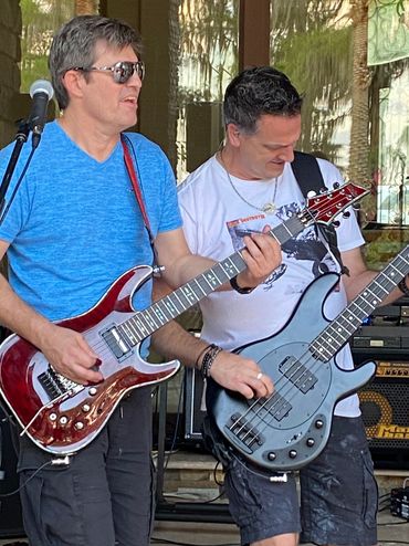 Two men passionately playing electric guitars during a live outdoor performance.