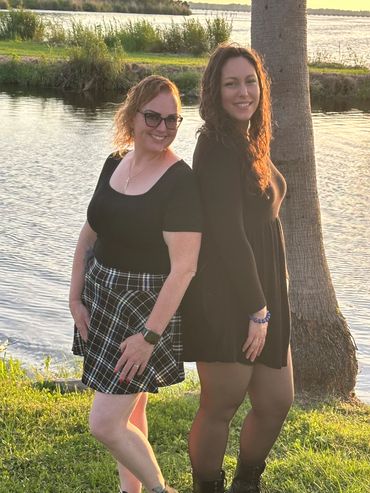 Two women posing back-to-back near a lakeside during golden hour.