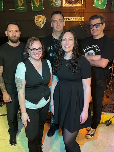 A group of five smiling adults posing in a music-themed room with Guinness banners.