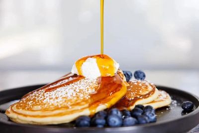 maple syrup pouring over pancakes with blueberries and cream. photo credit n. otto register