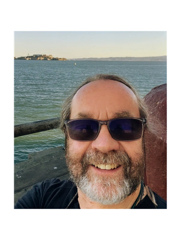 Man with sunglasses smiling by the waterfront on a clear day.