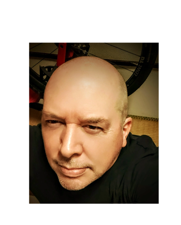 Close-up selfie of a bald man with a serious expression indoors.