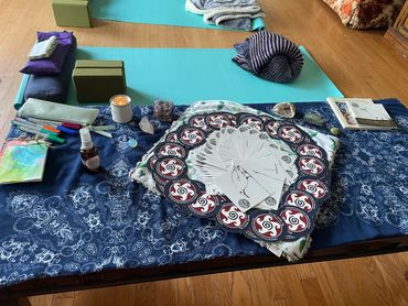 A table with yoga mats, tarot cards, candles, and crystals arranged for a spiritual session.