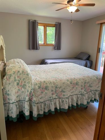A bedroom with a floral bedspread and a single gray bed near a window.
