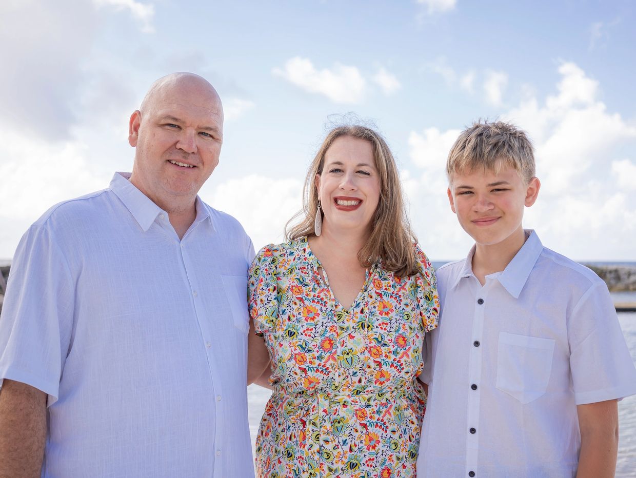 Smiling family of three posing by the water on a sunny day.