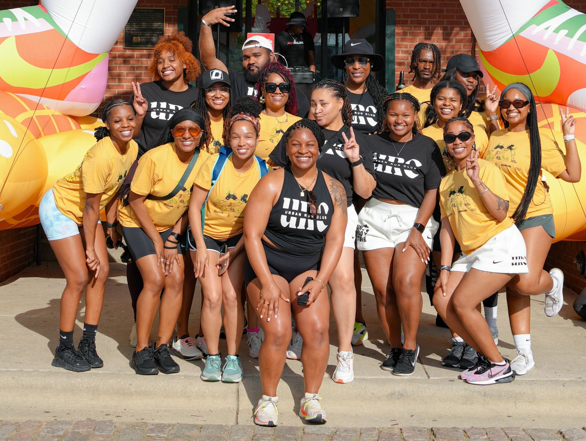 Group of smiling people posing outdoors in matching shirts and shorts.
