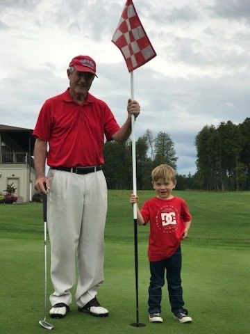 An elderly man and a young boy on a golf course holding a flagstick.