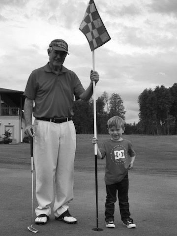 An elderly man and a young boy on a golf course holding a flagstick.