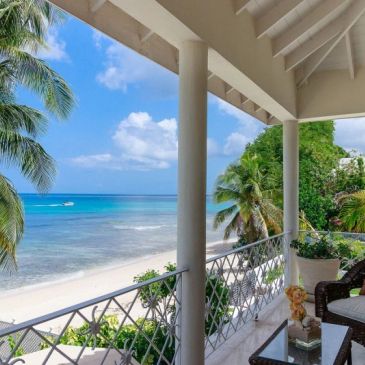 Beachfront balcony with tropical plants and ocean view.