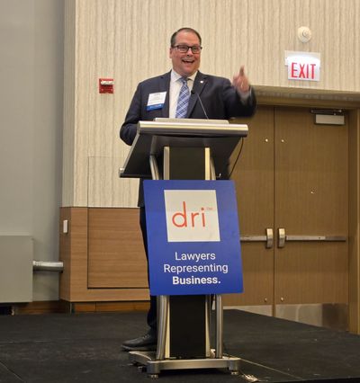 Man in business suit speaking at a podium with a DRI sign.