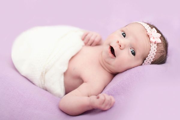 A newborn baby girl, with her eyes open and smiling at the camera, covered in a white blanket