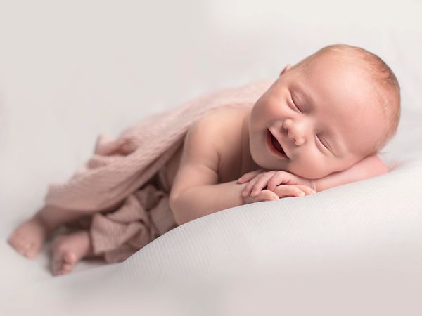 Lavender Cloud Photography a sleeping newborn baby posed naked with a smile and comfortable pose