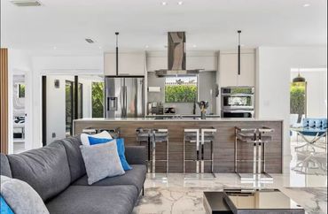 Modern open kitchen with stainless steel appliances and a gray sofa in the foreground.