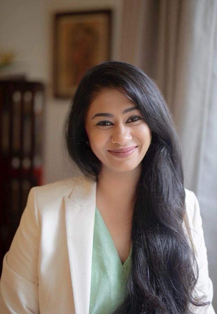 A woman looking into the camera, with a gentle smile. She has black long hair, swept to the side.