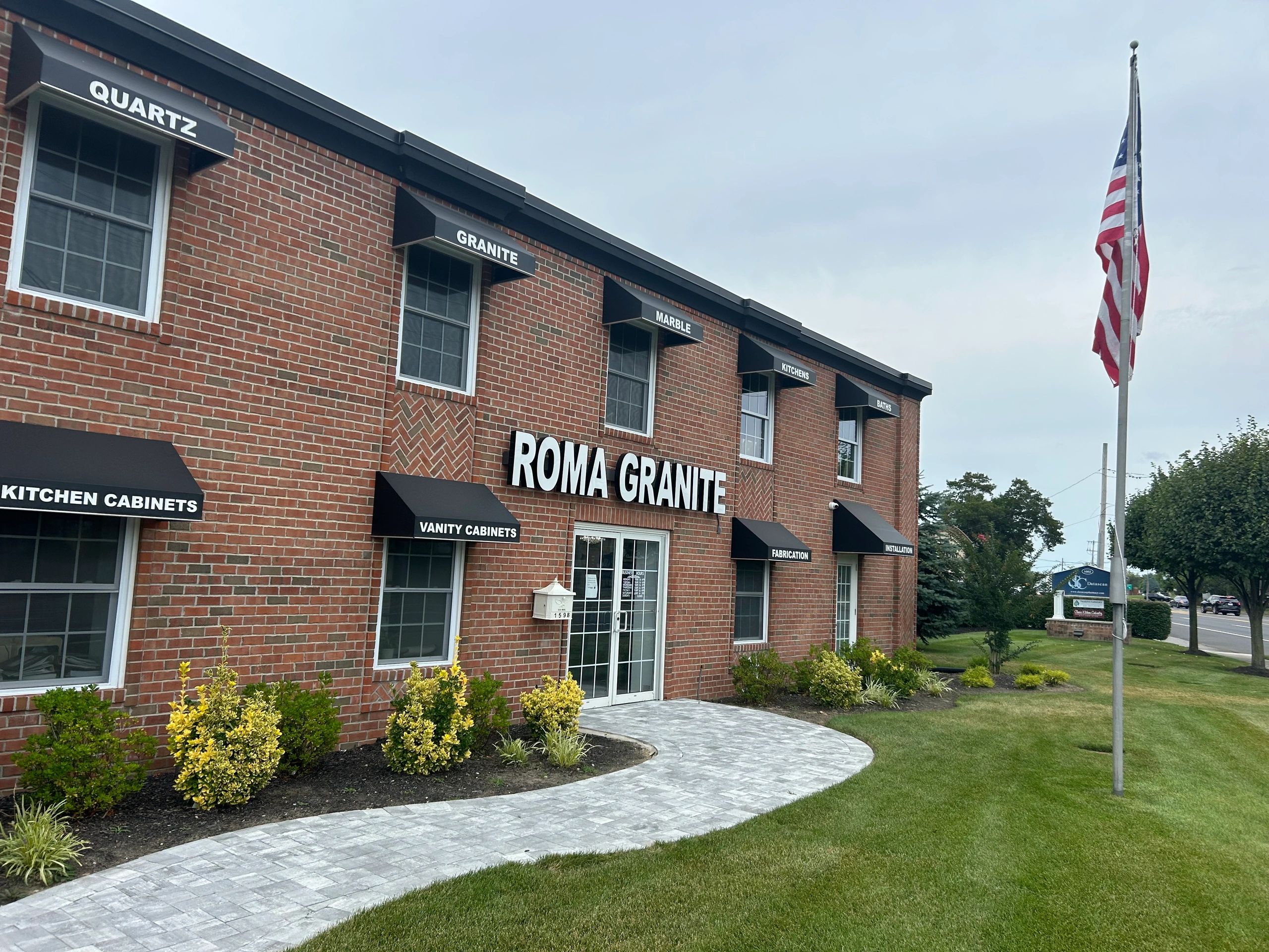 Exterior of Roma Granite building with American flag and landscaped lawn.