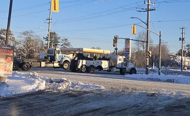 Snowy road with tow trucks and traffic lights under a clear blue sky.