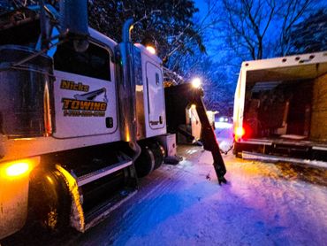 Nick's towing truck operating on a snowy road at dusk.
