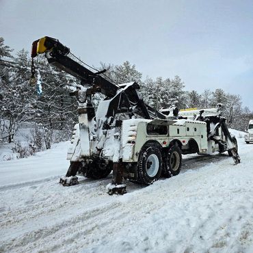 Heavy tow truck covered in snow on a snowy road.