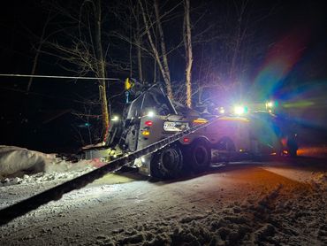 Tow truck pulling a vehicle on a snowy road at night.