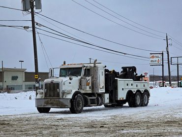 A white tow truck parked on a snowy, muddy lot under a cloudy sky.