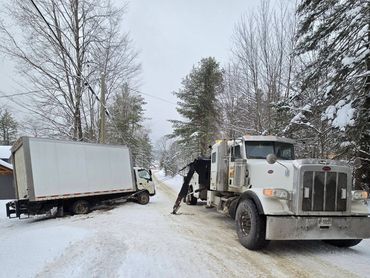 A tow truck pulls a stuck delivery truck from a snowy ditch.