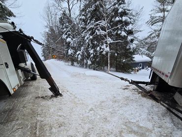 A tow truck pulling a stuck box truck on a snowy road.