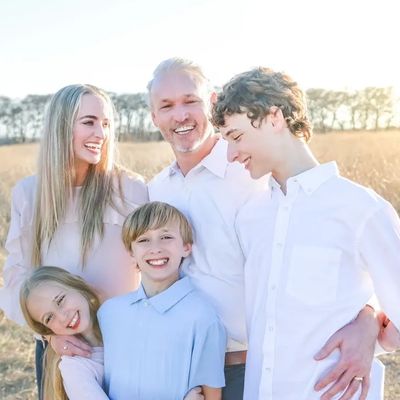 A happy family of five smiling in a sunlit field.