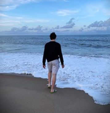 Person walking on a beach towards the ocean under a cloudy sky.