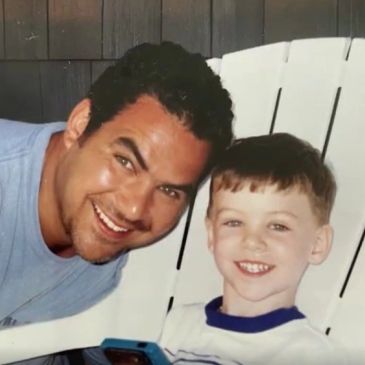 Smiling man and child sitting on a white chair.