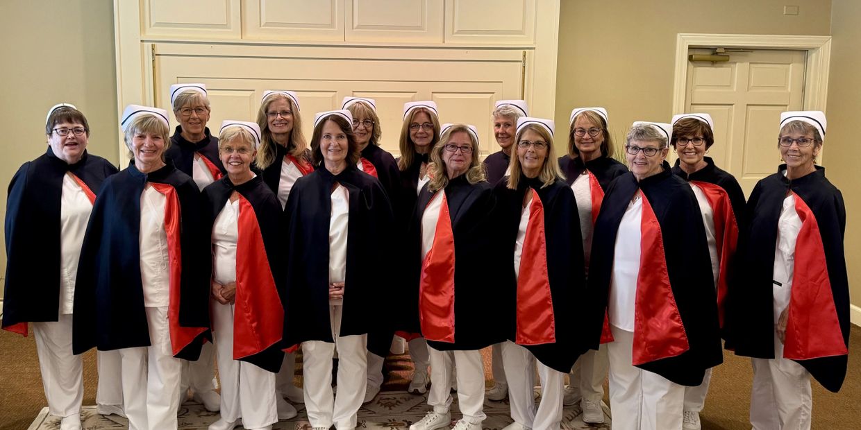 Group of women in vintage nurse uniforms with black capes and white caps.
