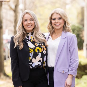 Two smiling women in blazers standing outdoors on a sunny day.