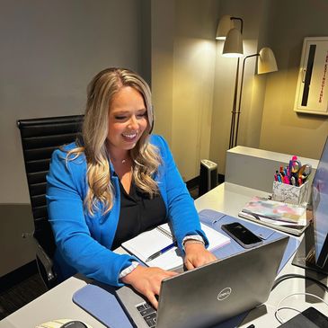 Woman in blue blazer working on a laptop at a well-organized office desk.