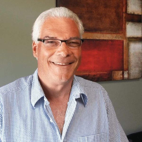 Smiling elderly man with glasses in a checkered shirt.